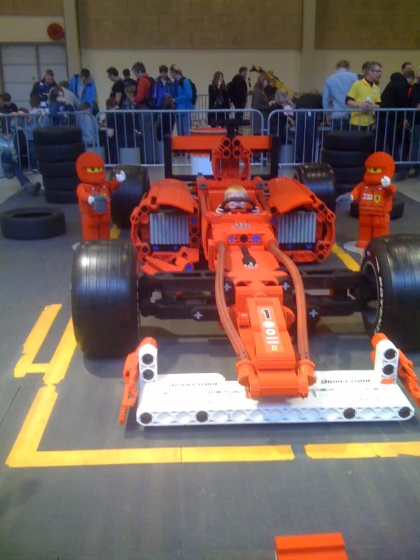 A large red LEGO racing car with a child behind the wheel